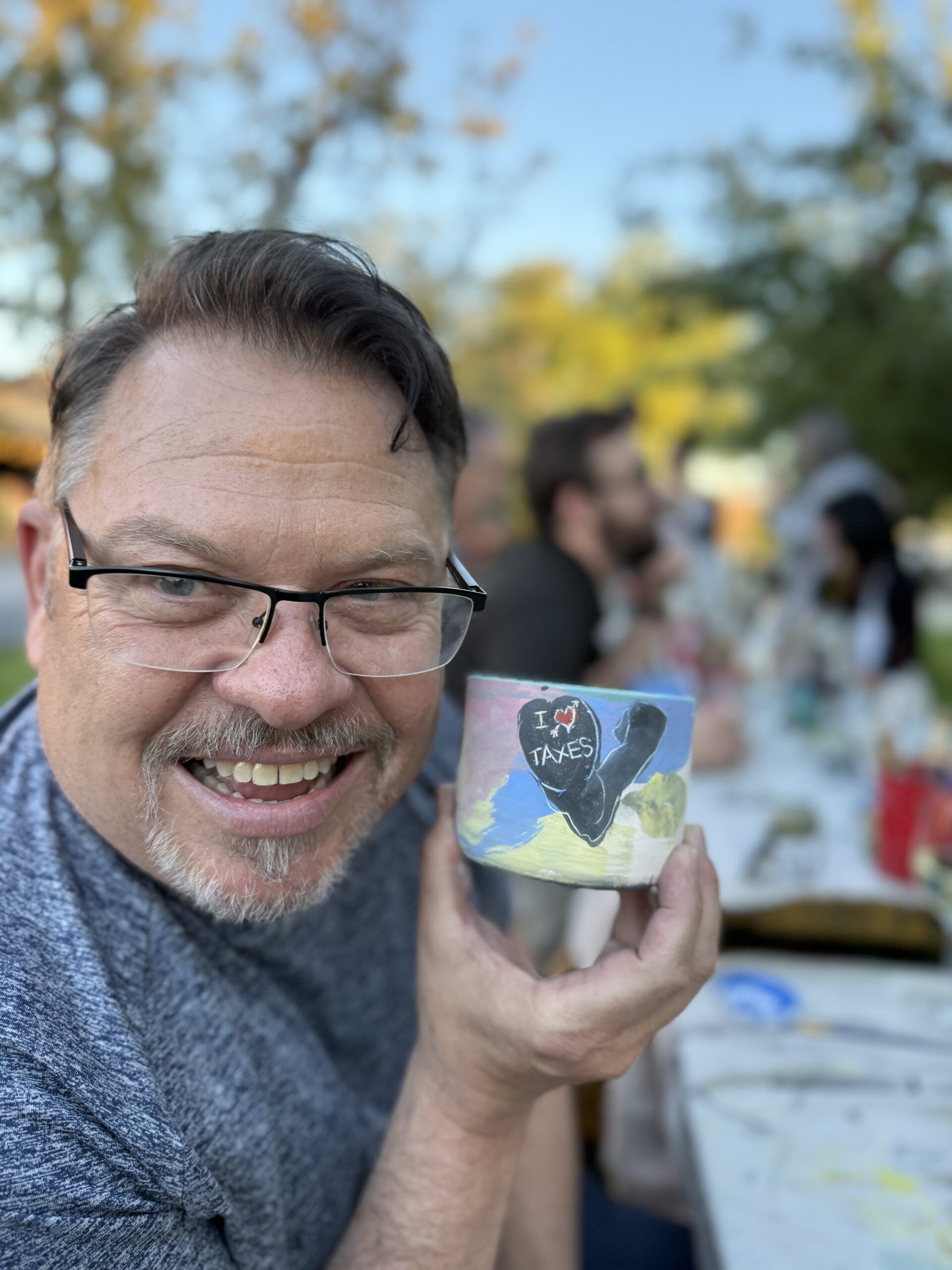 John Warekois holding up a handmade mug that says "I love taxes"