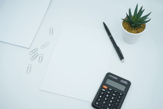 Blank paper, paper clips, calculator, and plant on white table